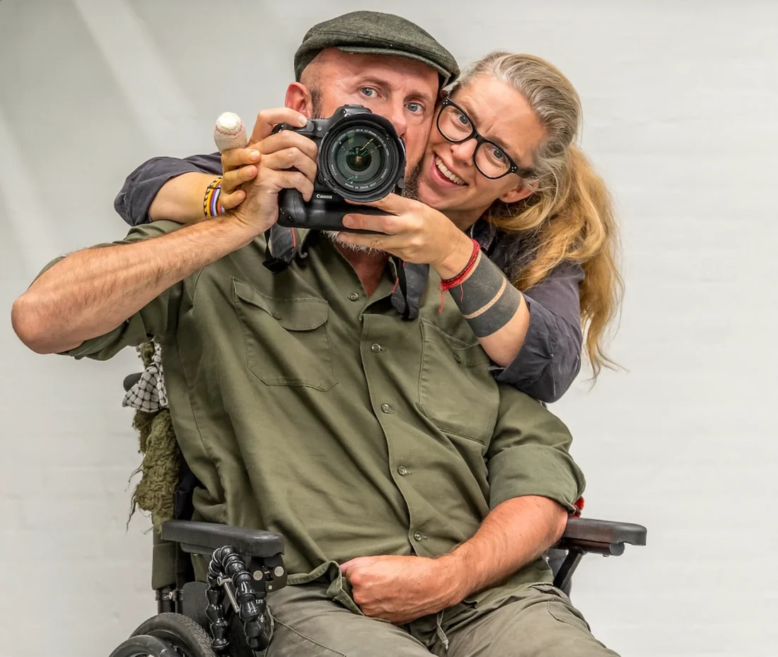 Uri Løvevild Golman with a camera to his eye, his wife Helle beside him, her arms around him